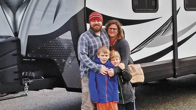 A father, mother and their two boys pose for a family photo in front of their RV, which is hitched to their pickup truck.