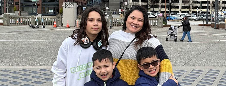 Image of BECU employee Marybeth with her husband, Jose, and their three children, (from left) Ayden, Derek and Nathan smiling for a photo outside. A rocky beach is pictured in the background.