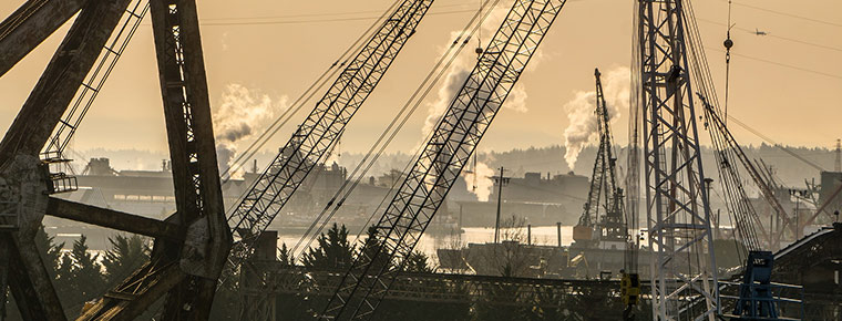 Cranes and bridges along the Lower Duwamish Waterway with steam plumes from industry operations in the background. The sky is brown and hazy from wildfire smoke.