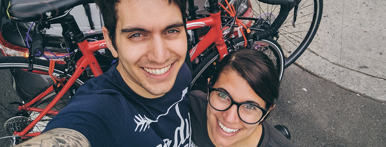 A couple smiling, taking a selfie. A pair of bicycles are on a car-mounted bike rack in the background.