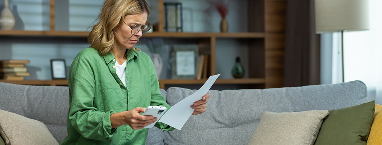 Upset woman looking at paperwork and holding mobile phone