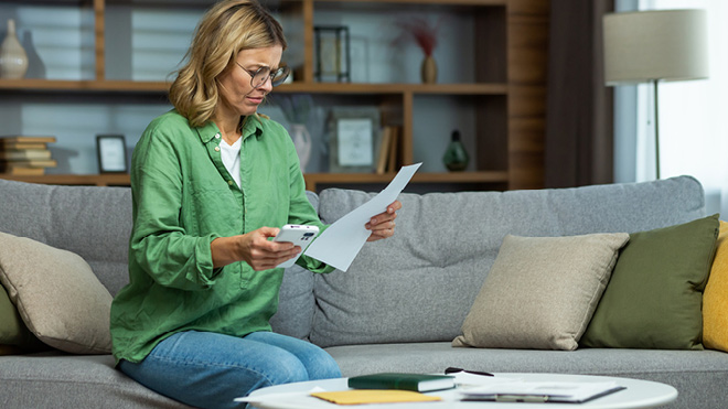Upset woman looking at paperwork and holding mobile phone