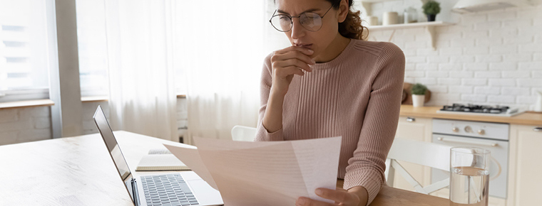Concerned woman sitting at laptop looking at paperwork