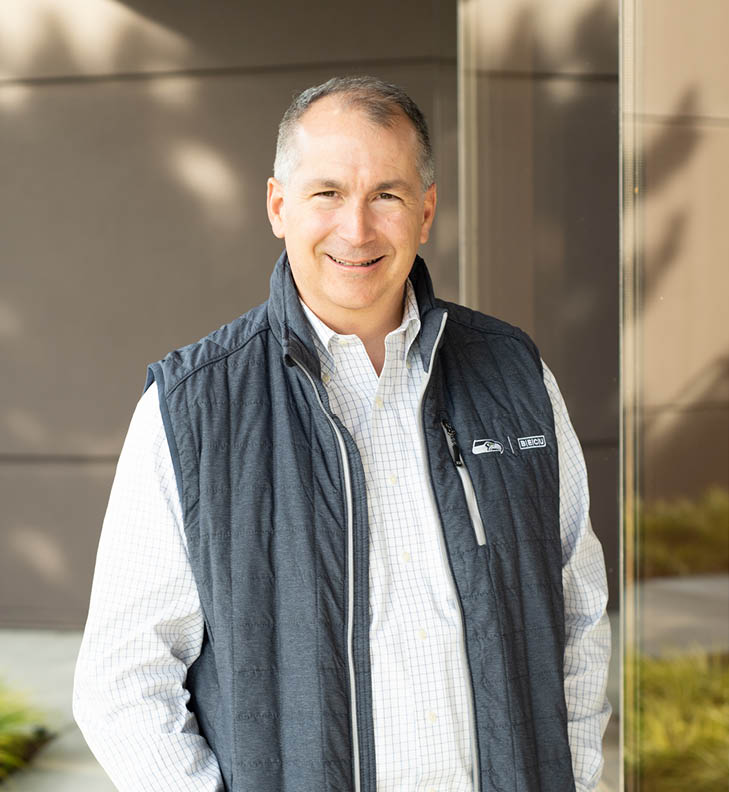 BECU CEO Benson Porter smiling, standing outside BECU headquarters, wearing a zippered vest and button down shirt.