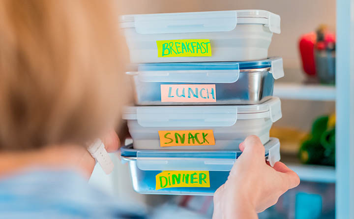 A person places a stack of labeled plastic food containers into a refrigerator.